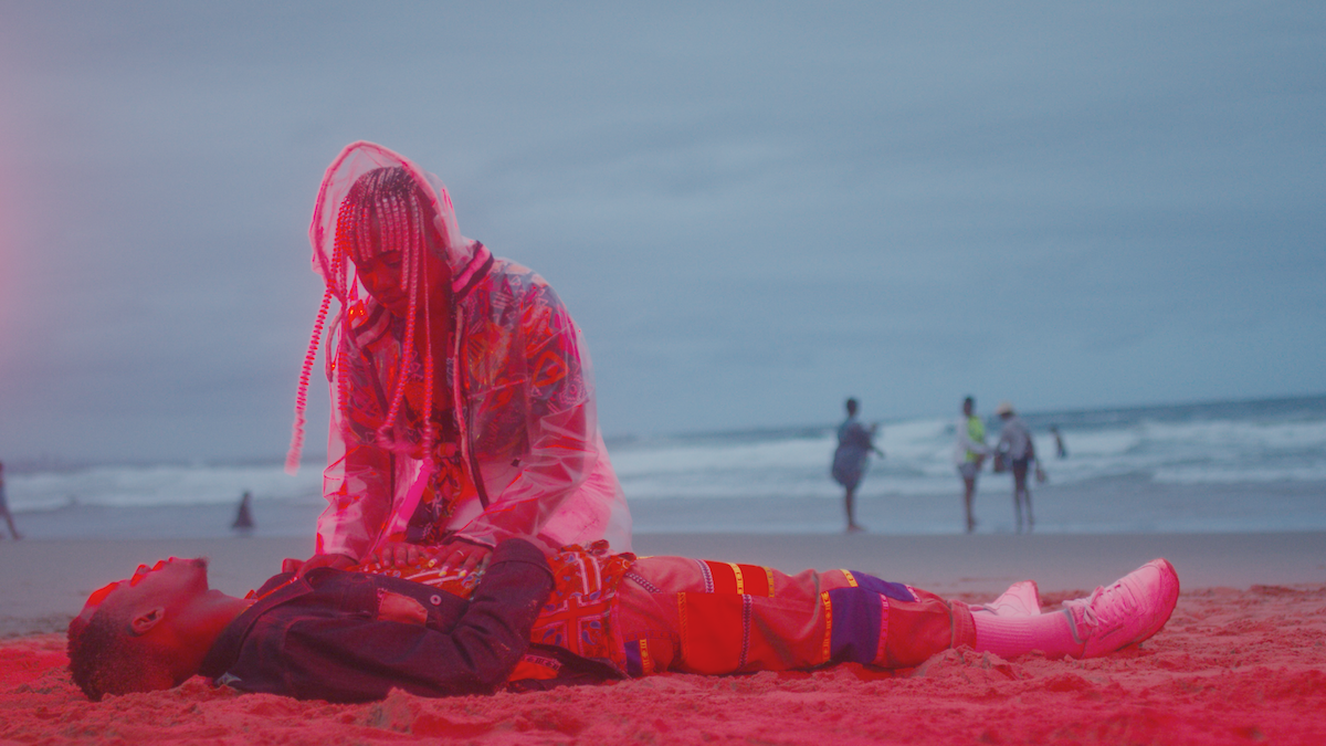 Juliet kneeling next to Romeo who's laying at the beach. 