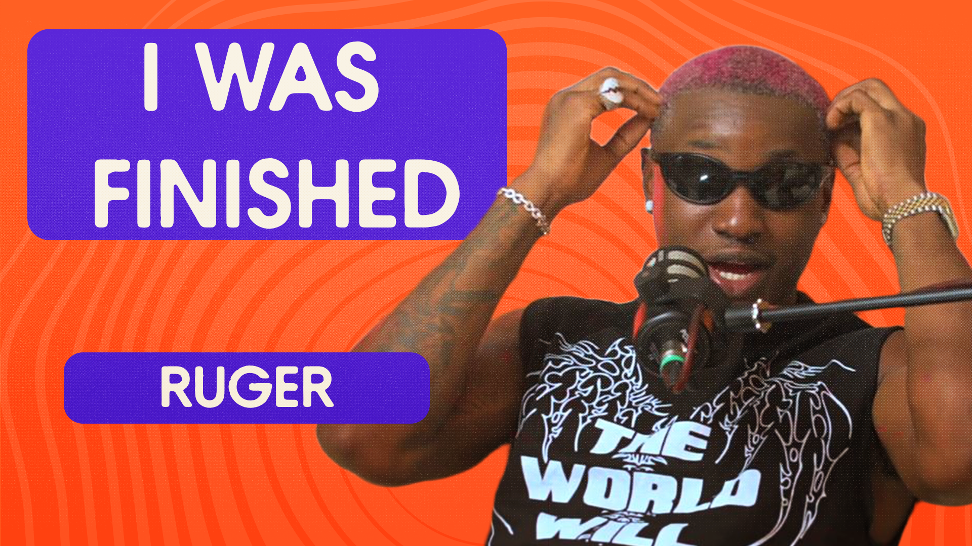 Ruger speaking into a microphone during a podcast interview, wearing sunglasses and a black sleeveless shirt with the text 'THE WORLD WILL'. 