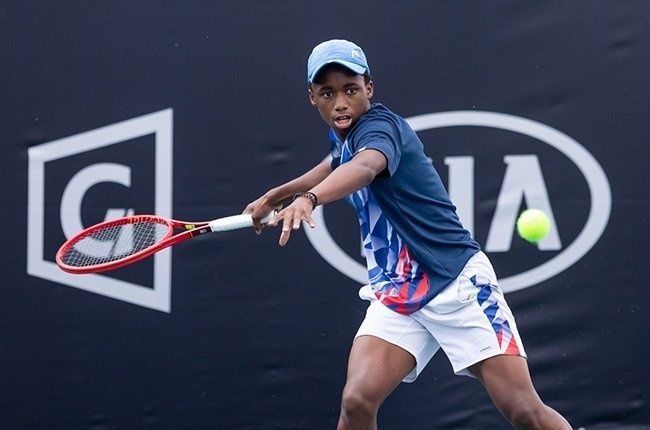 Young black man playing tennis wearing white shorts and blue top.