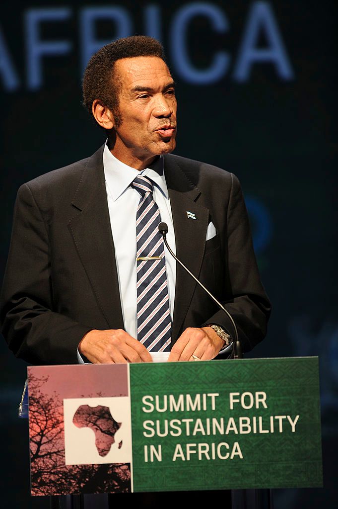 President of Botswana Ian Khamastanding behind podium wearing blue suit with striped tie about deliver speech.