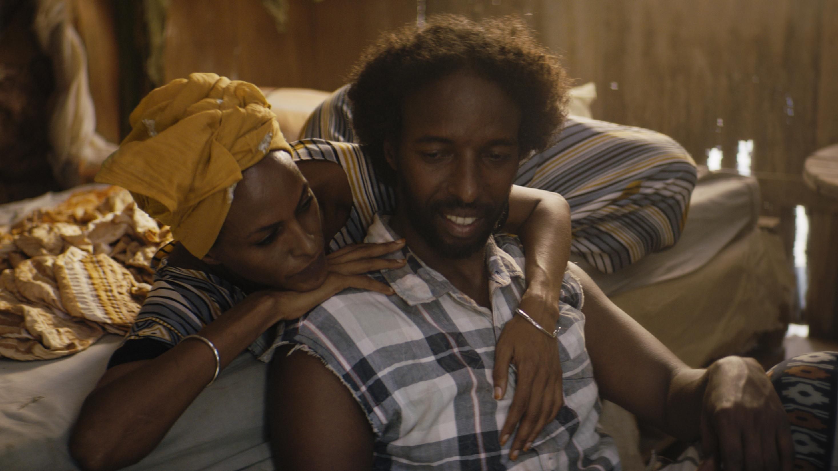 A still from the film, The Gravedigger's Wife, of a woman lying in bed with her arms around a man who's sitting on the floor