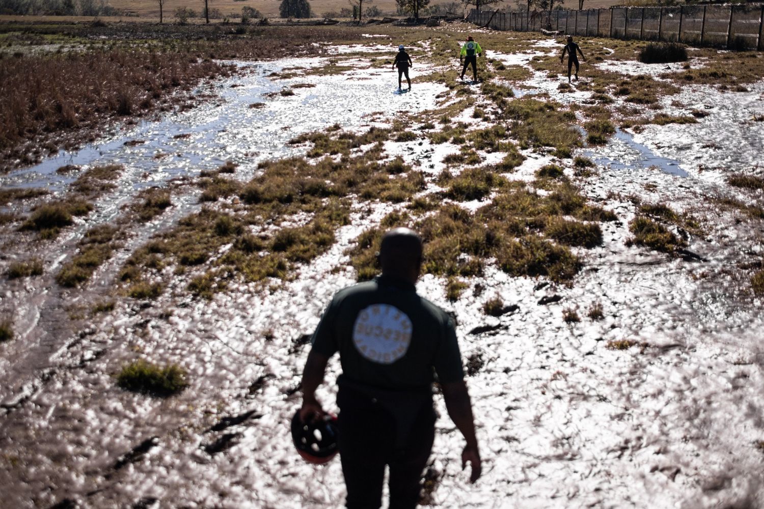 Rescue workers walk across a flooded and muddy field in a rural area. 