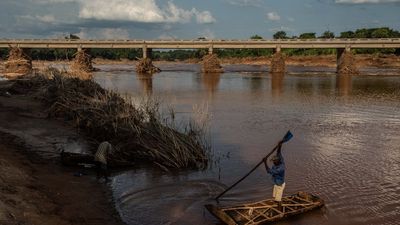 A photo of a man paddling a boat across the Lucite River after the bridge was damaged during Cyclone Idai, on March 26, 2019, outside of Magaro, Mozambique.