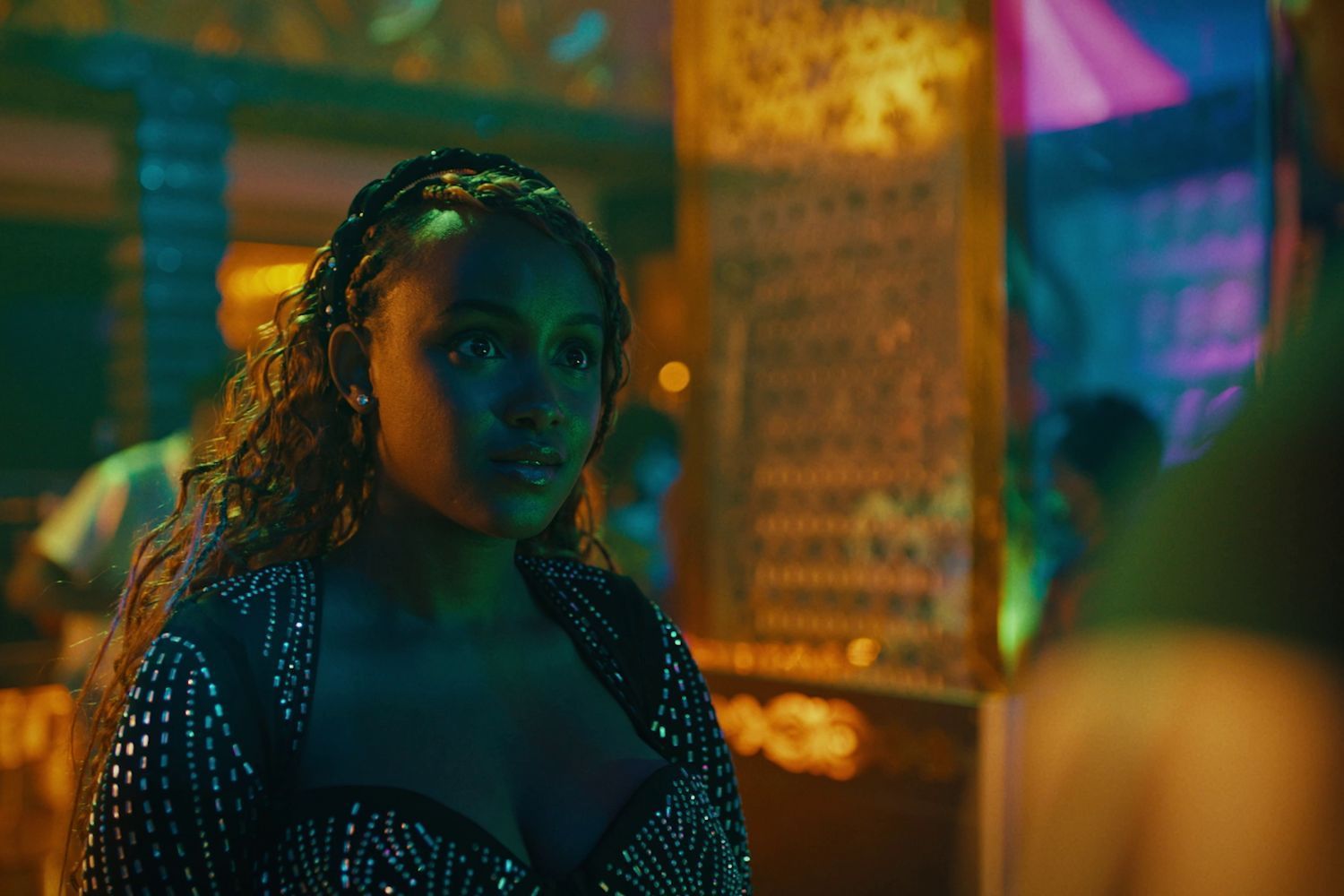 A young woman stands in a neon-lit club, looking focused 