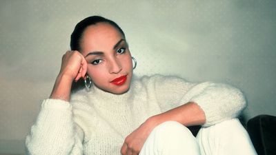 Singer Sade Adu poses for a portrait while sitting down wearing all white outfit.