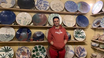 Ibrahim Samir stands in front of shelves of decorative plates in his workshop in Tunis. 
