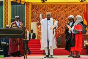 President Mahama poses with his hand raised while reading off a piece of paper behind a large background made from kente fabric.