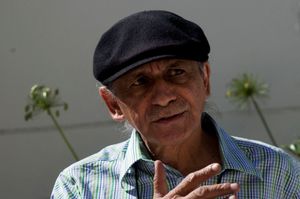 Rashid Lombard, director and co-founder of the Cape Town International Jazz Festival, wearing a checkered shirt and Irish cap, gesticulates as he speaks.