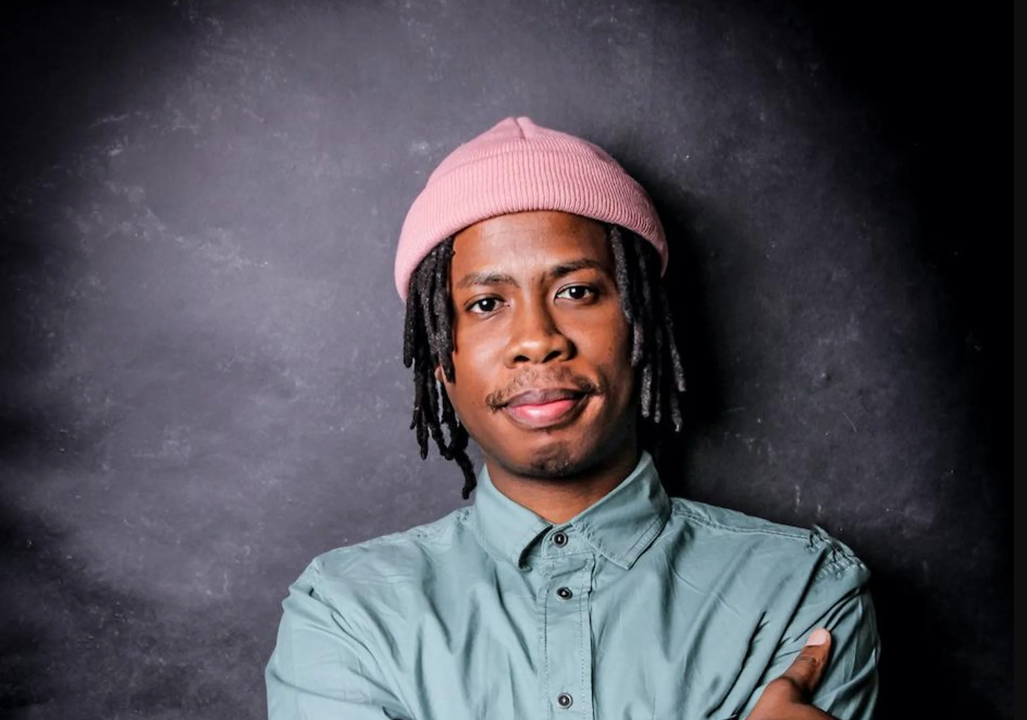 A portrait of Masande Ntshanga wearing a green shirt to a black backdrop. 