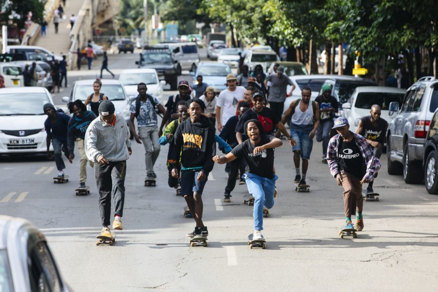 A group of skateboarders ride down a city street in Nairobi, surrounded by traffic and onlookers, capturing the energy and unity of the local skateboarding scene.
