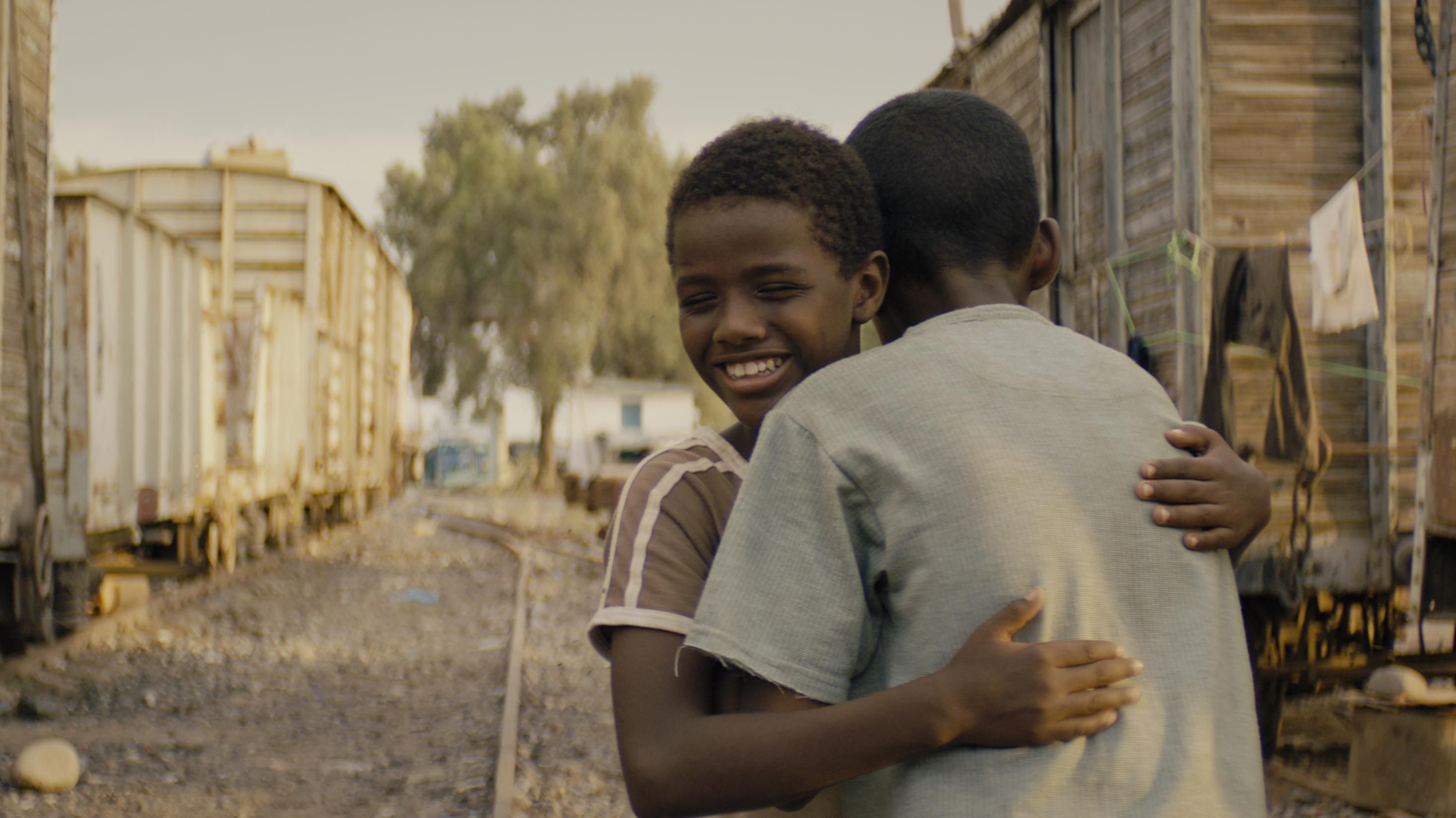 A film still of a boy hugging another boy