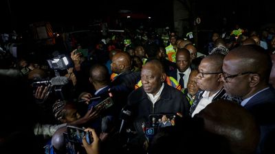 South African President Cyril Ramaphosa (C) speaks to journalists at the scene where more than 70 people were killed in a building fire in Johannesburg on August 31, 2023. A fire that tore through a five-storey building taken over for illegal housing killed 74 people including 12 children in central Johannesburg overnight, South African authorities said August 31, 2023. 