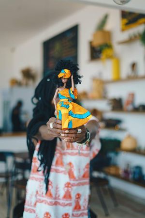 An image of a woman blurred and holding a doll wearing an African print dress.