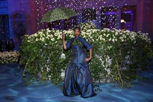 Tems in a blue Ankara suit dress with a puff skirt accented with a green cravat and a matching umbrella.