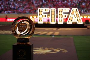 The FIFA Club World Cup 2025 Winner’s Trophy is displayed in the foreground on a black pedestal. Behind it, large illuminated letters spell out “FIFA” against the backdrop of a crowded stadium.
