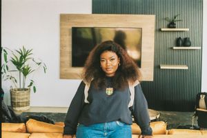 Thando Zide looks directly at the camera in a promo shoot. She wears a black sweater and blue jeans.