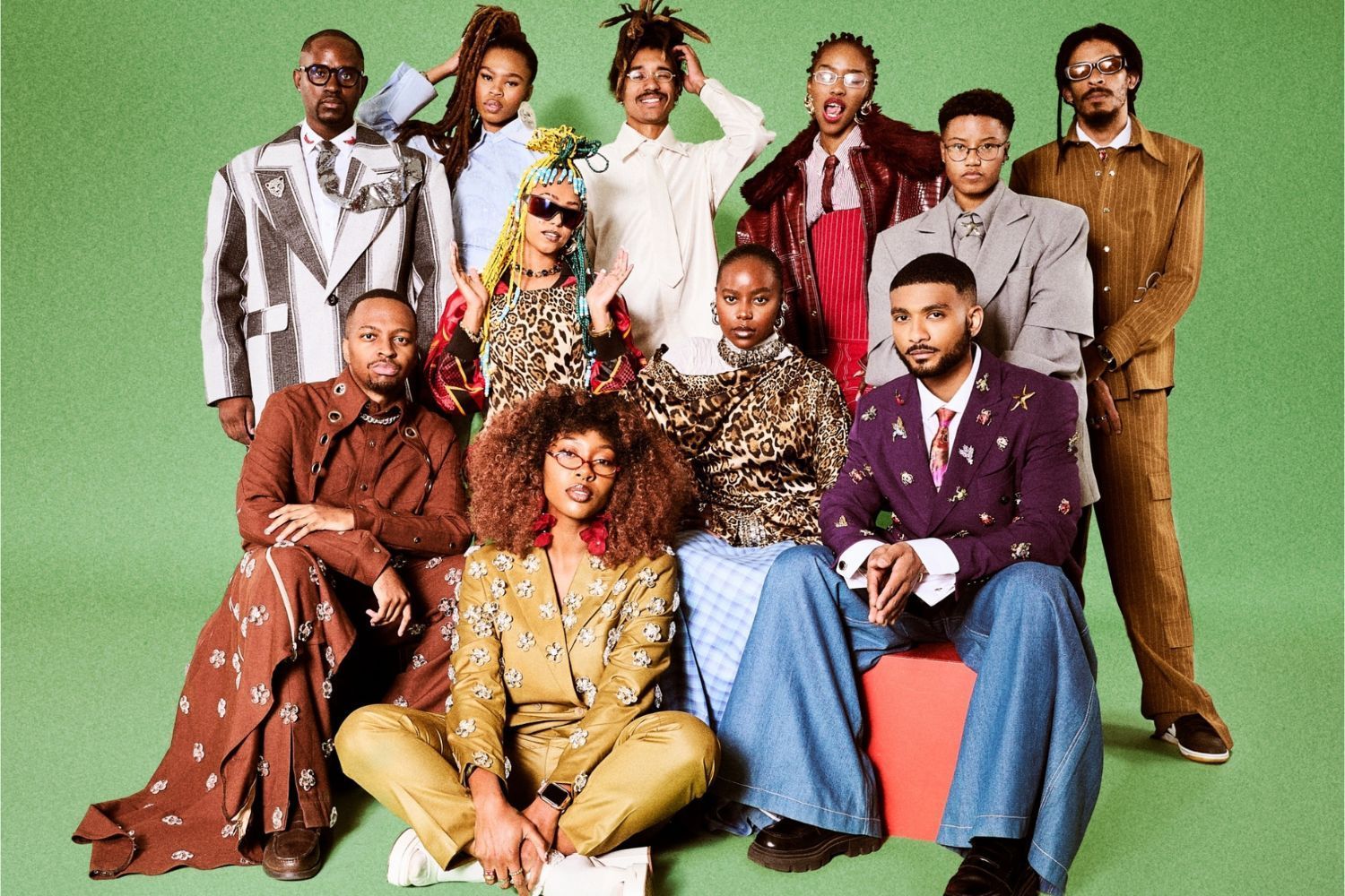Group portrait of stylishly dressed young Black creatives posing against a green backdrop.