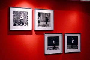Four black-and-white photographs are framed and displayed on a vivid red wall. Each photo captures a stylish portrait of an individual standing or posing against bold, patterned backdrops, evoking a retro or studio aesthetic. The arrangement and contrast highlight African identity and vintage visual culture.