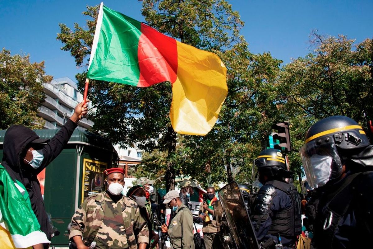 Man waving Cameroonian flag facing armed men with shields and helmets 