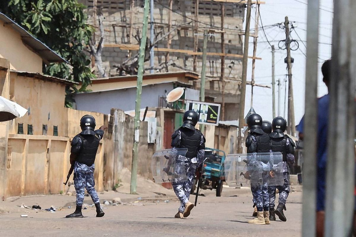 Members of the Togolese Gendarmerie in riot gear and machine guns facing away from the camera on an empty street