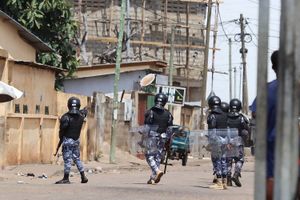 Members of the Togolese Gendarmerie in riot gear and machine guns facing away from the camera on an empty street