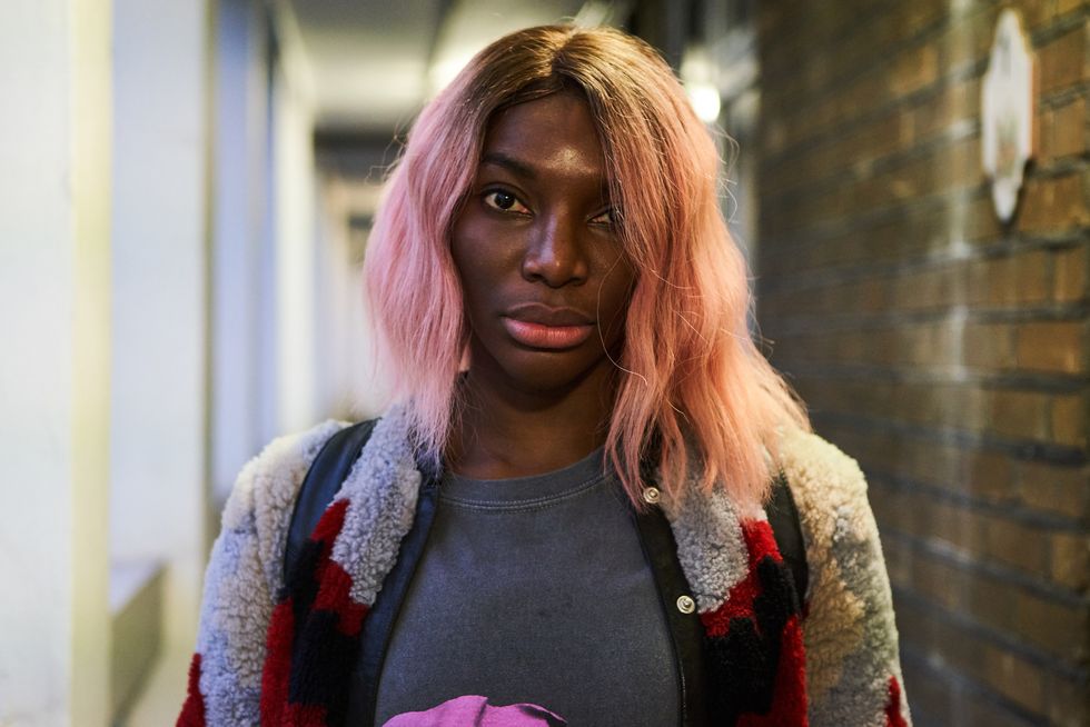 Michaela Coel in pink hair and fleece jacket looking at the camera.