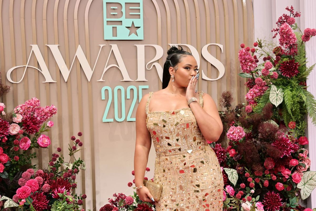 Moliy wears a gold embellished gown and poses on the red carpet at the 2025 BET Awards, blowing a kiss in front of a floral backdrop.