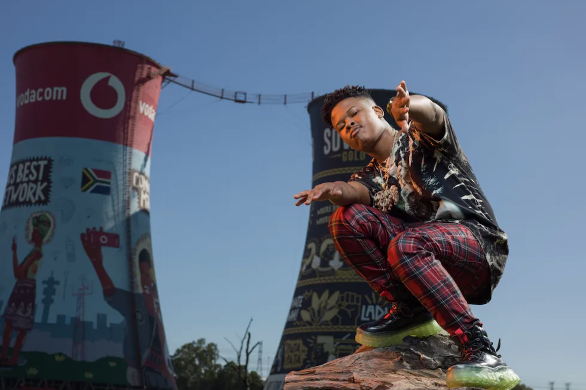 Nasty C posing on a rock to a backdrop of the Soweto skyline. 