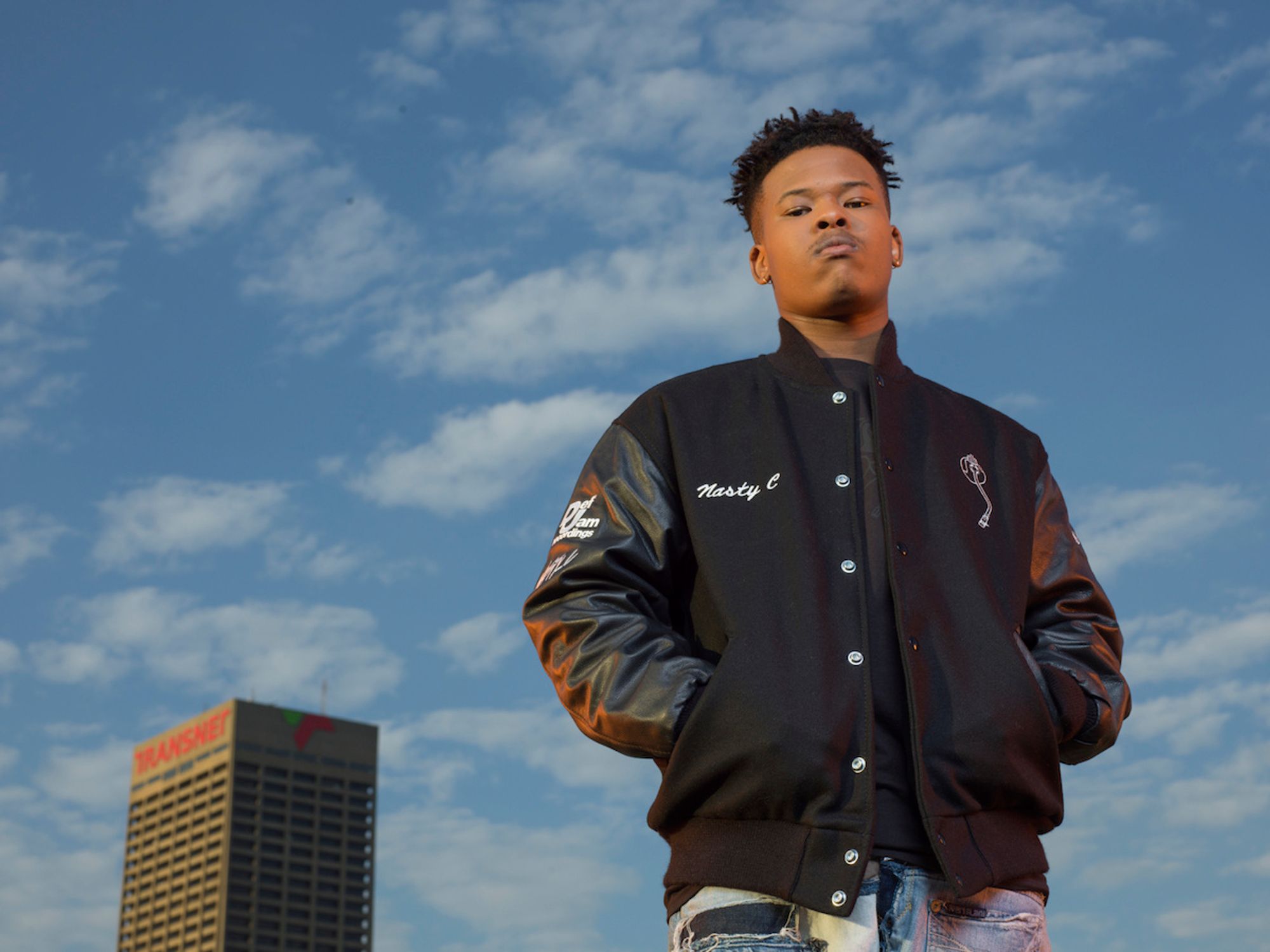 Nasty C posing to a background of clouds and the sky. 