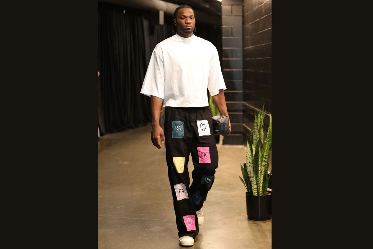 NBA player Precious Achiuwa pictured mid-walk while wearing patchwork black pants and a white tee.