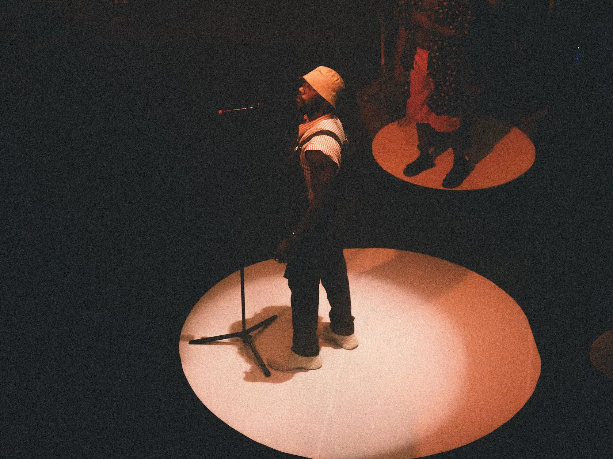Nigerian artist AYLO stands in front of a mic in a dark room lit by a white circle.