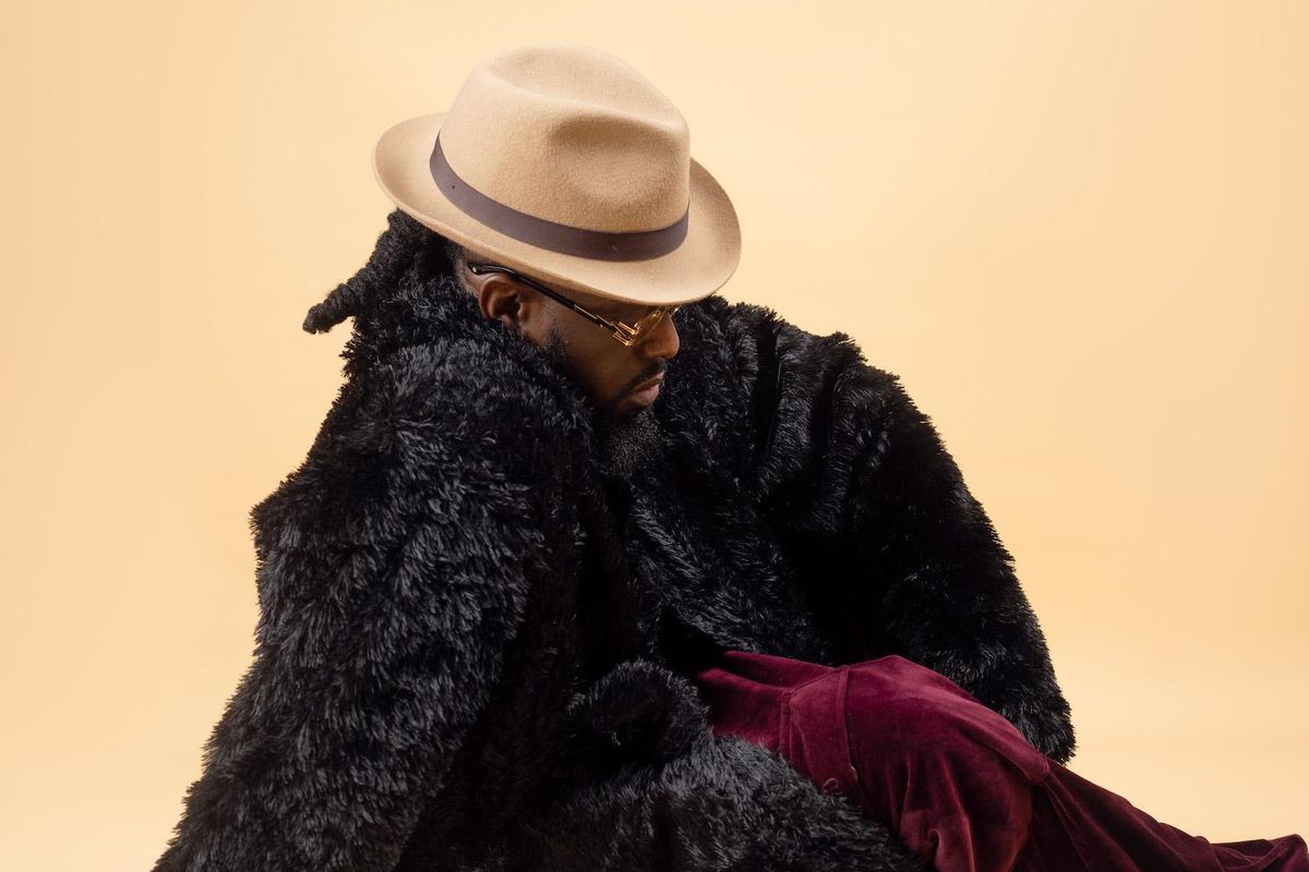 Nigerian artist Timaya sits in a yellow background with a black fur coat.