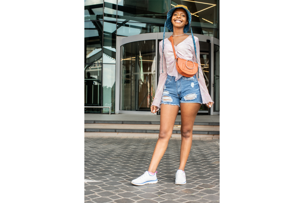 Patricia Rakhudu wears a bucket hat and jean shorts and smiles for the camera.