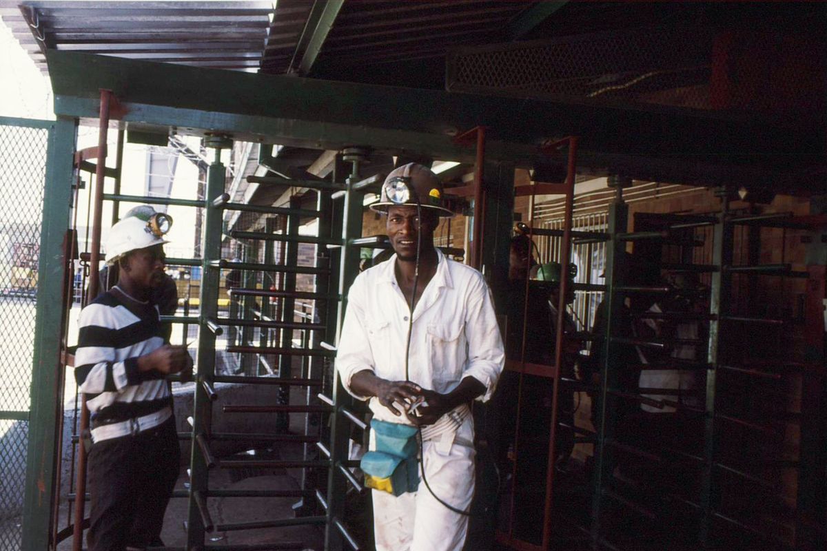 Platinum mineworker in white overalls looks apprehensively into the camera