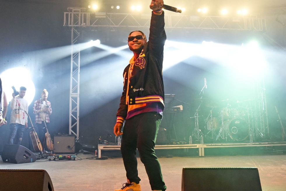 Poco Lee performs on stage at the SXSW festival. He is rocking shades, with one hand holding a mic in the air.