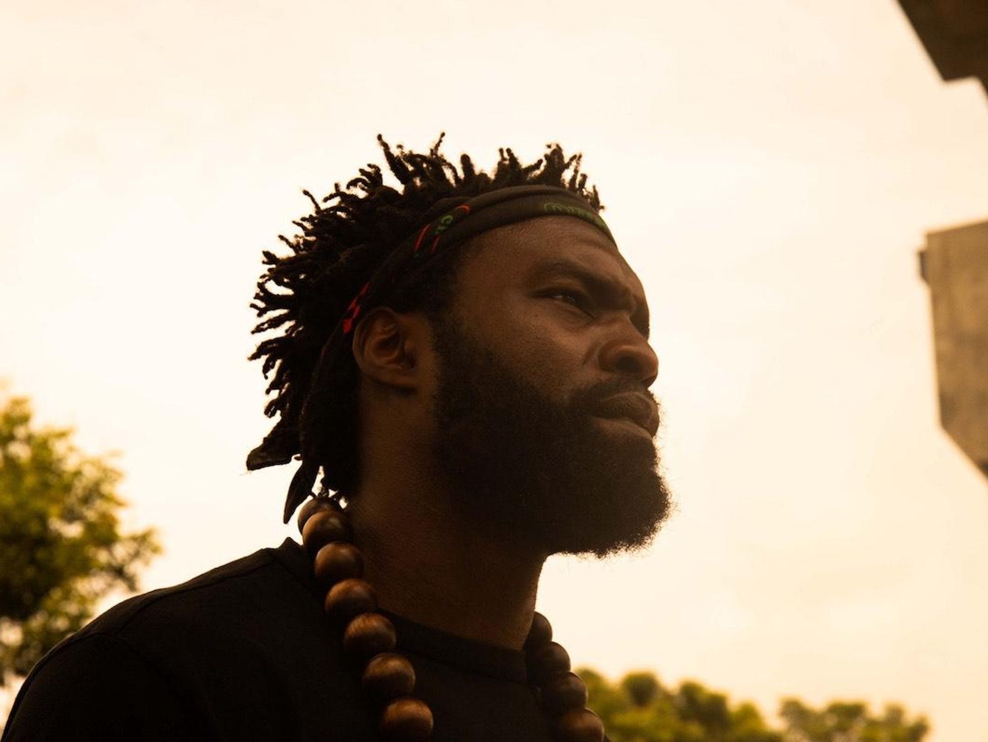 Profile picture of music video director Meji Alabi. He wears a bandana on his forehead and large bead necklace over black t-shirt.