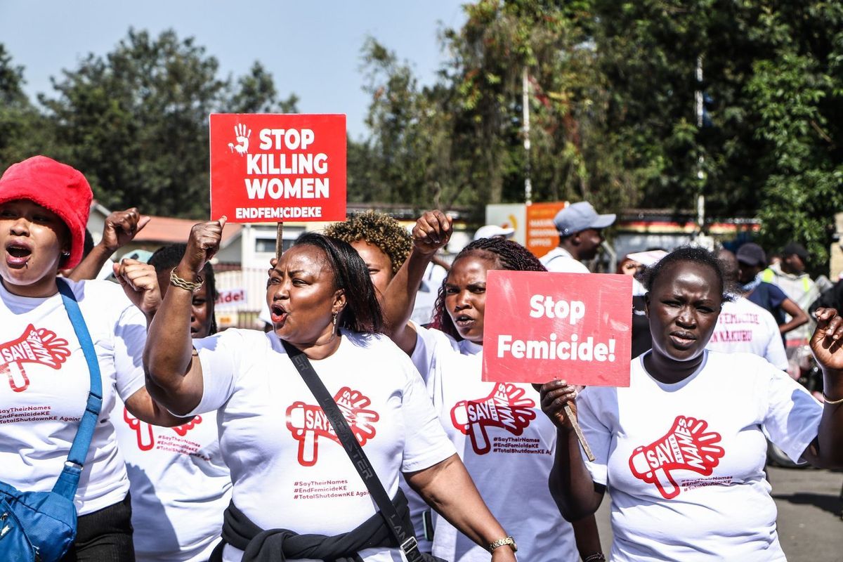 Several women are protesting and chanting, wearing white t-shirts and holding up red posters that read “stop killing women.”