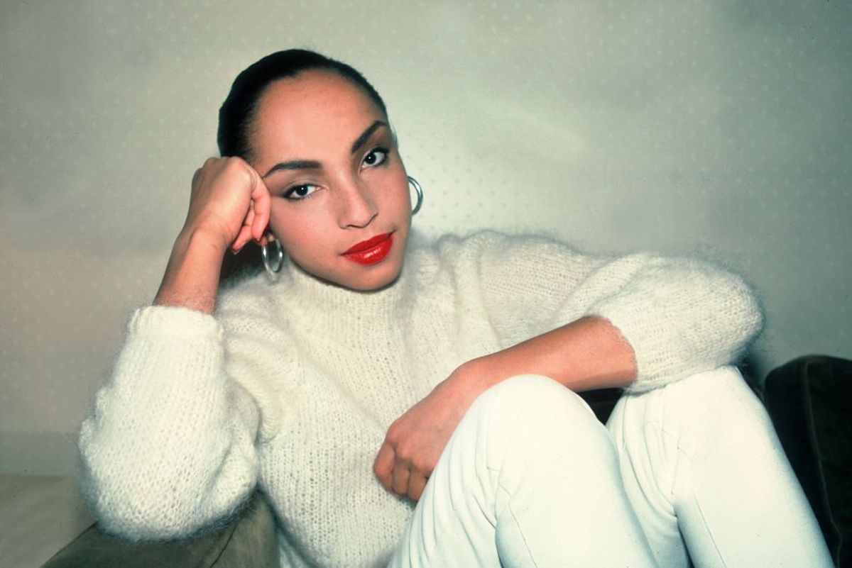 Singer Sade Adu poses for a portrait while sitting down wearing all white outfit.