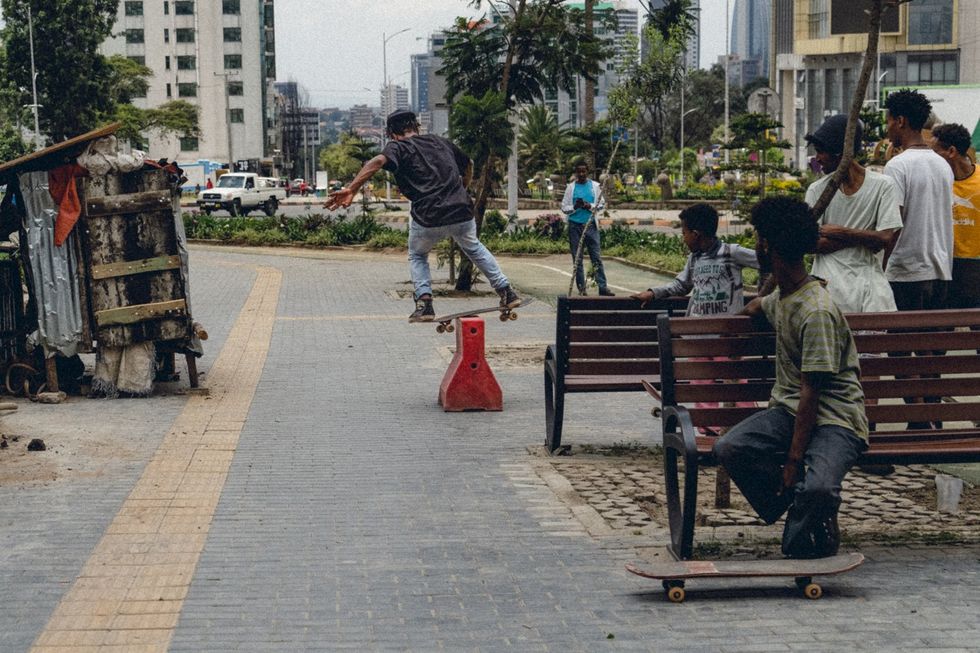 Skateboarders watch another jump an obstacle in the road.
