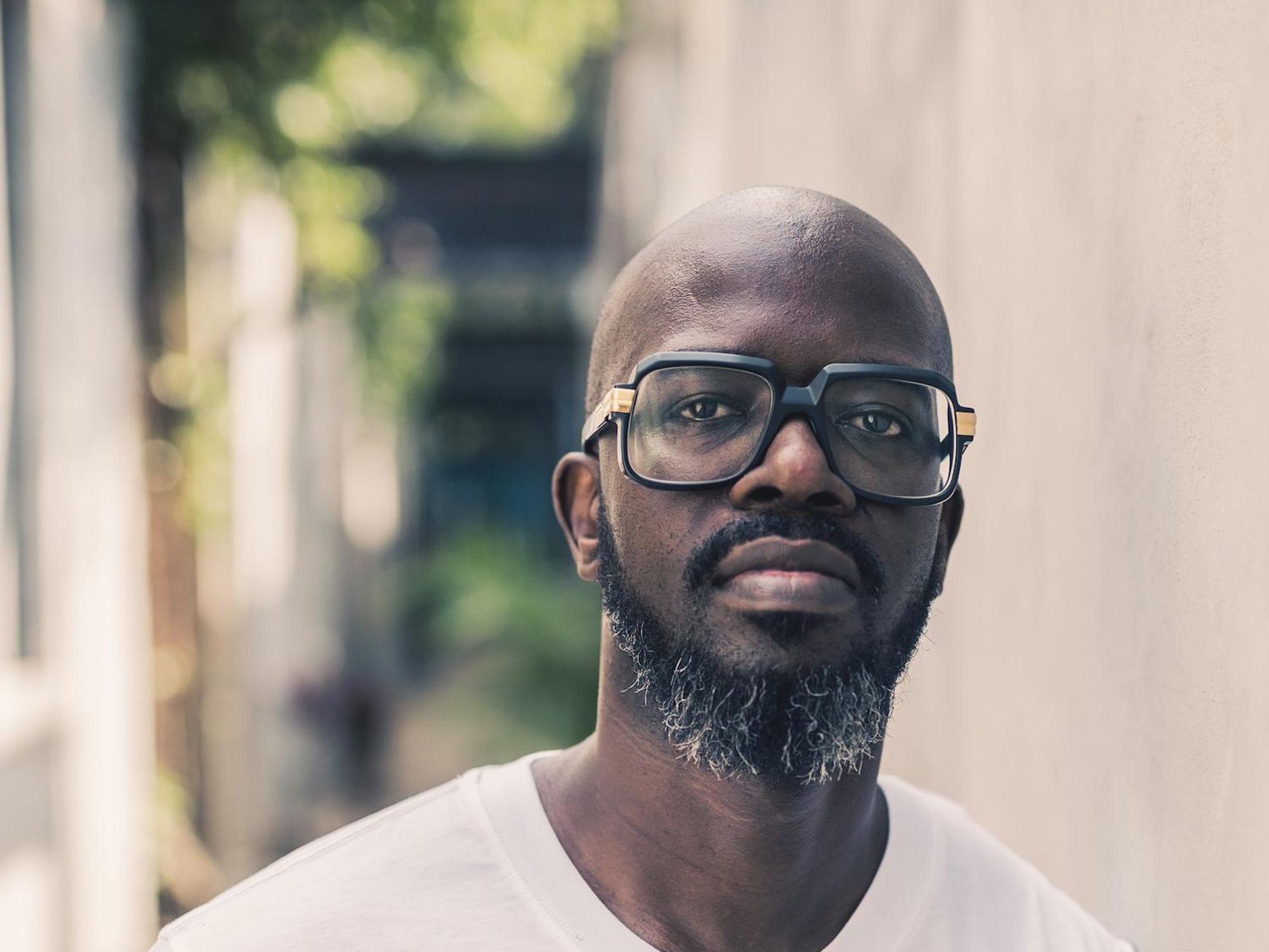 South African DJ Black Coffee stands, wearing a white tee shirt and clear glasses. 