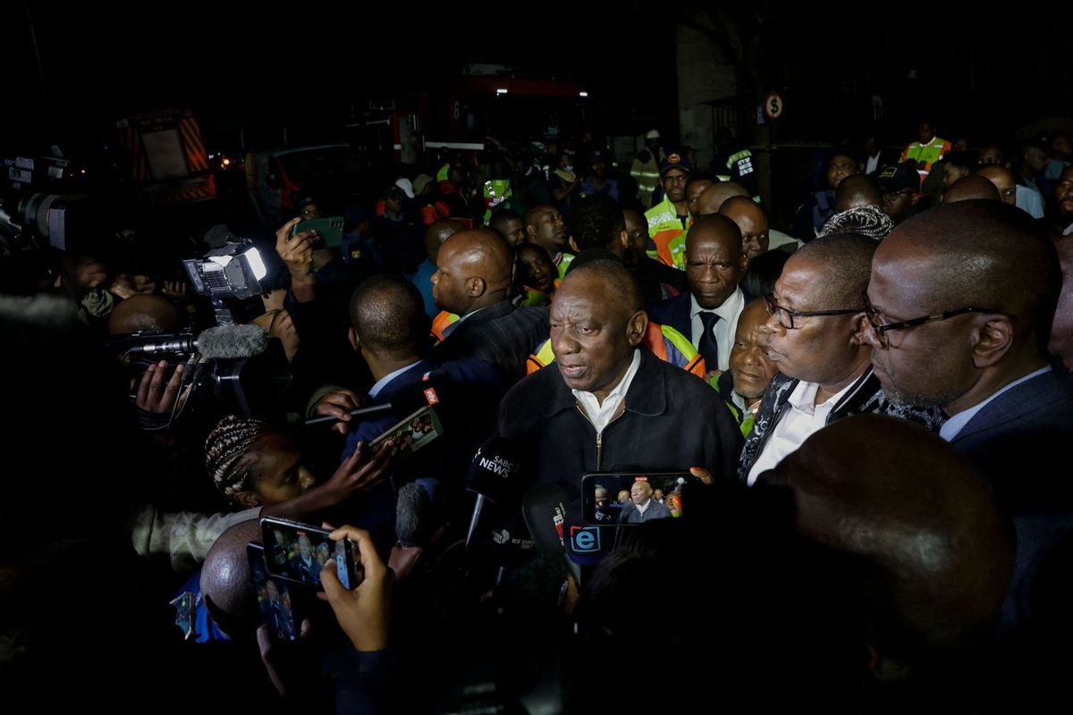South African President Cyril Ramaphosa (C) speaks to journalists at the scene where more than 70 people were killed in a building fire in Johannesburg on August 31, 2023. A fire that tore through a five-storey building taken over for illegal housing killed 74 people including 12 children in central Johannesburg overnight, South African authorities said August 31, 2023. 