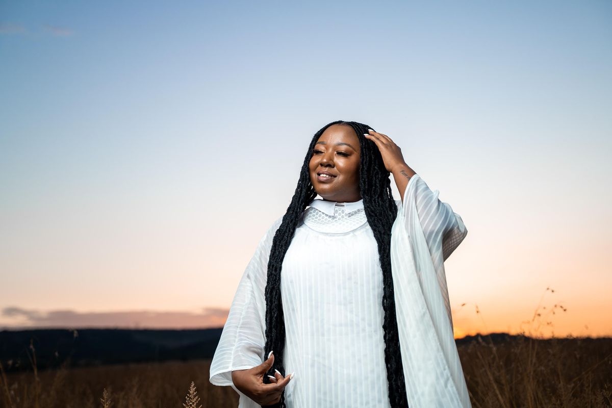 South African singer Brenda Mtambo shot in white on an open field. 
