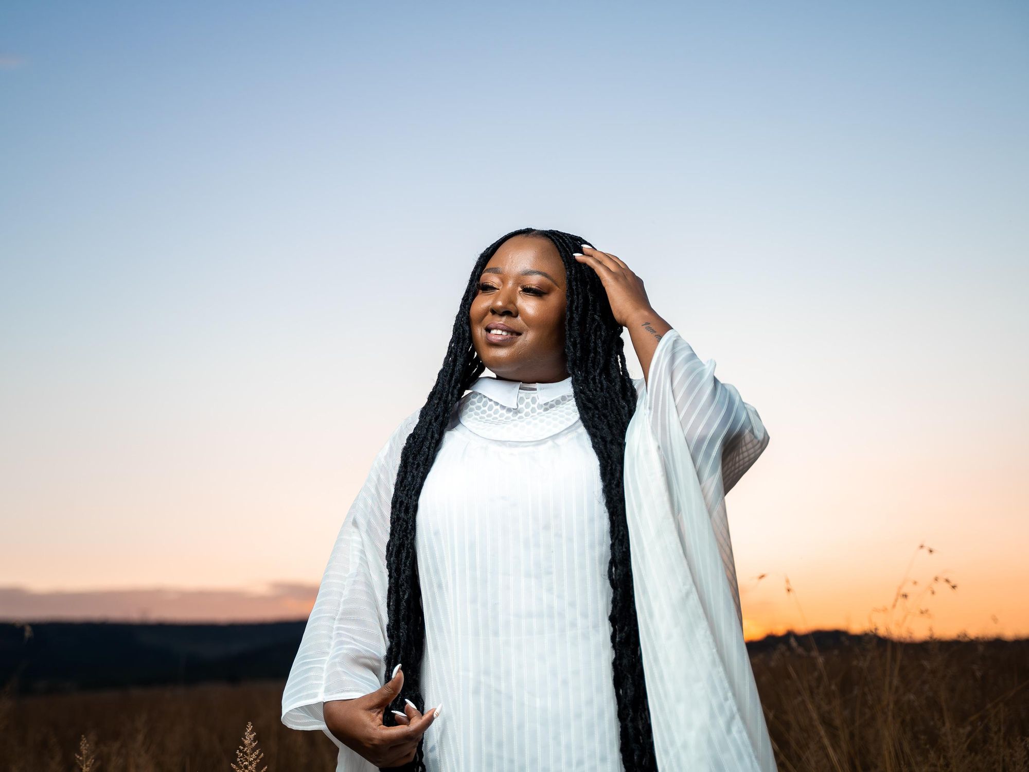 South African singer Brenda Mtambo shot in white on an open field. 