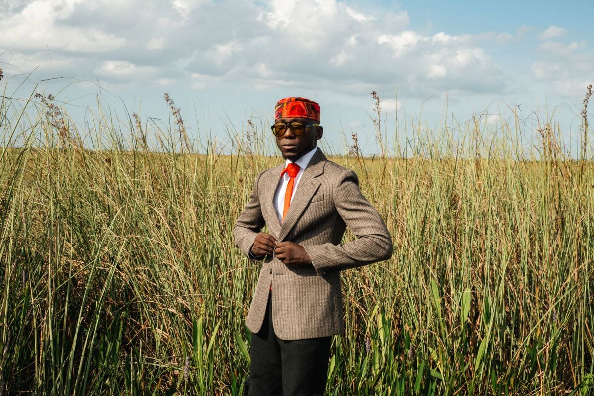 SPINALL wears his signature cap, posing in front of a shrub of grass