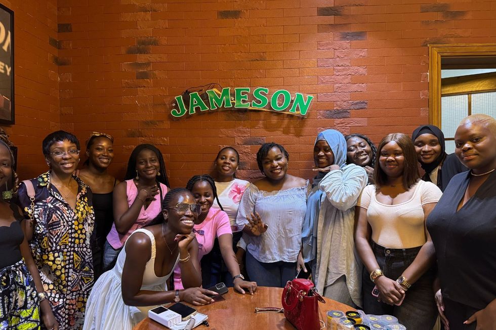 Stephanie Chisom Ozuo poses for a picture alongside participants at a career workshop organized in partnership with Black Girls in Tech Nigeria and Jameson. Theyu2019re standing in front of a brick wall with the Jameson logo on it.