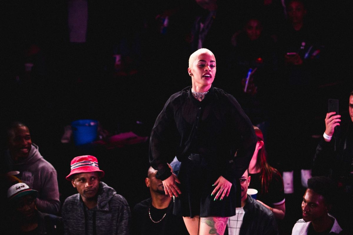 Tarryn Alberts catches a breath during a competition. Her face is flooded by red light, she is dressed in all black, and has short, blonde hair.