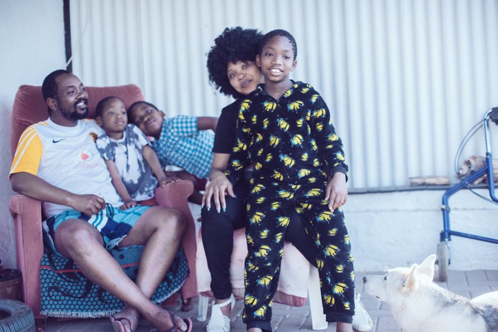 The Moletsane family hanging out during the weekend. A kid in pajamas sits on his mother's knee. A father sits in a chair with two other children in the background. 