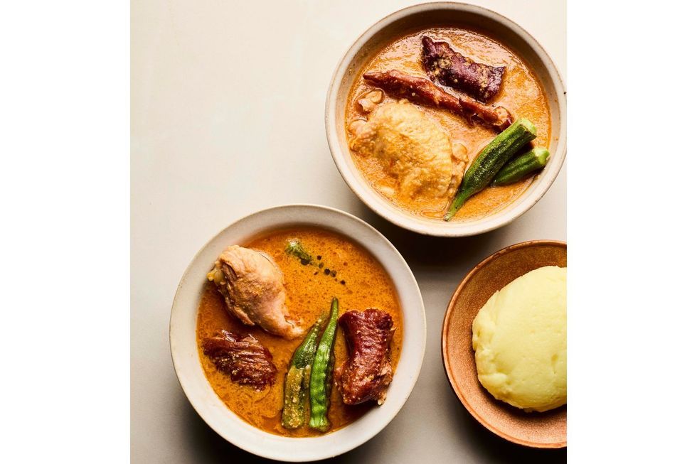 Two bowls of West African groundnut soup with meat, okra, and vegetables served alongside white pounded yam or fufu.