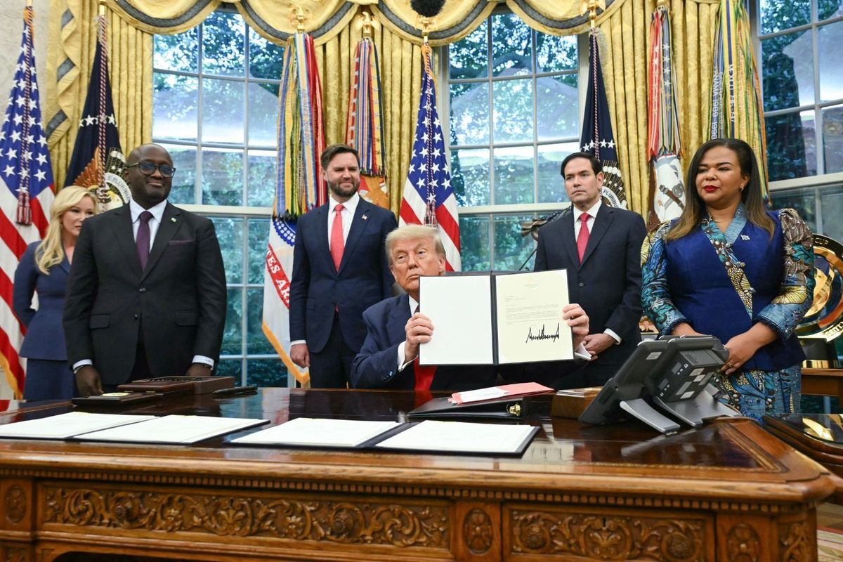 U.S. President Donald Trump stilling behind desk in Oval Office holds up the peace deal bearing his signature while Olivier Nduhungirehe, Rwanda's foreign minister, US Vice President JD Vance, Marco Rubio, US Secretary of State, and Therese Kayikwamba Wagner, Democratic Republic of the Congo foreign minister, are standing and look on.