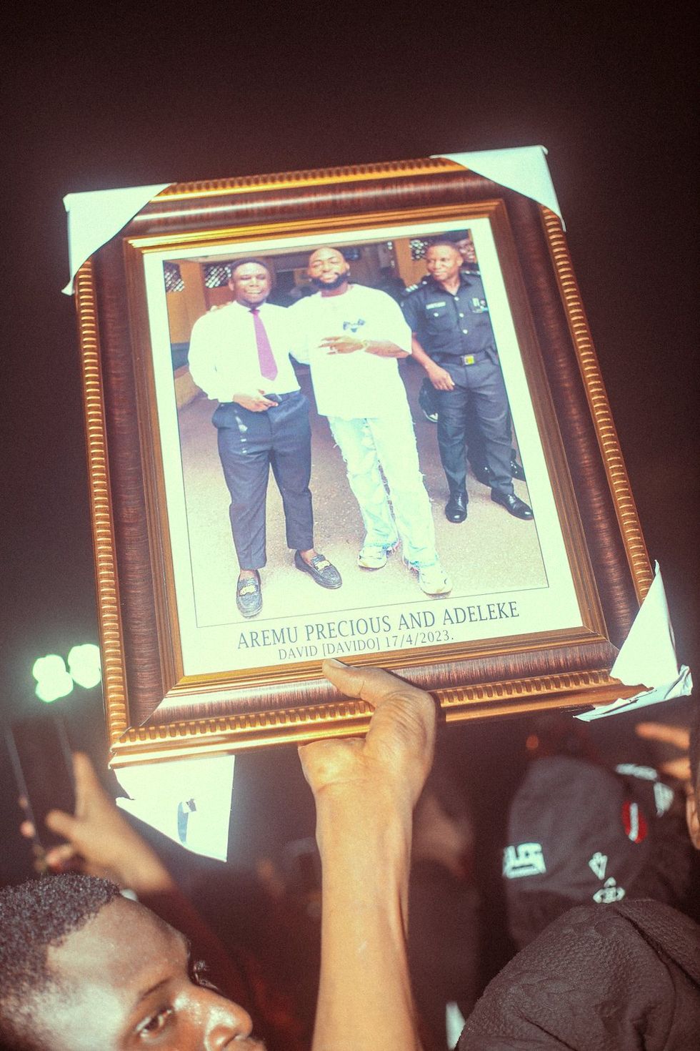 u200bA man (Aremu Precious) holds a framed picture of himself and Davido at the concert.